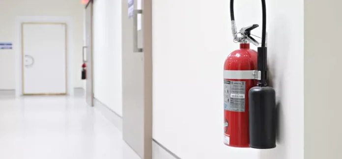 Fire extinguisher mounted on the wall of a white hallway.
